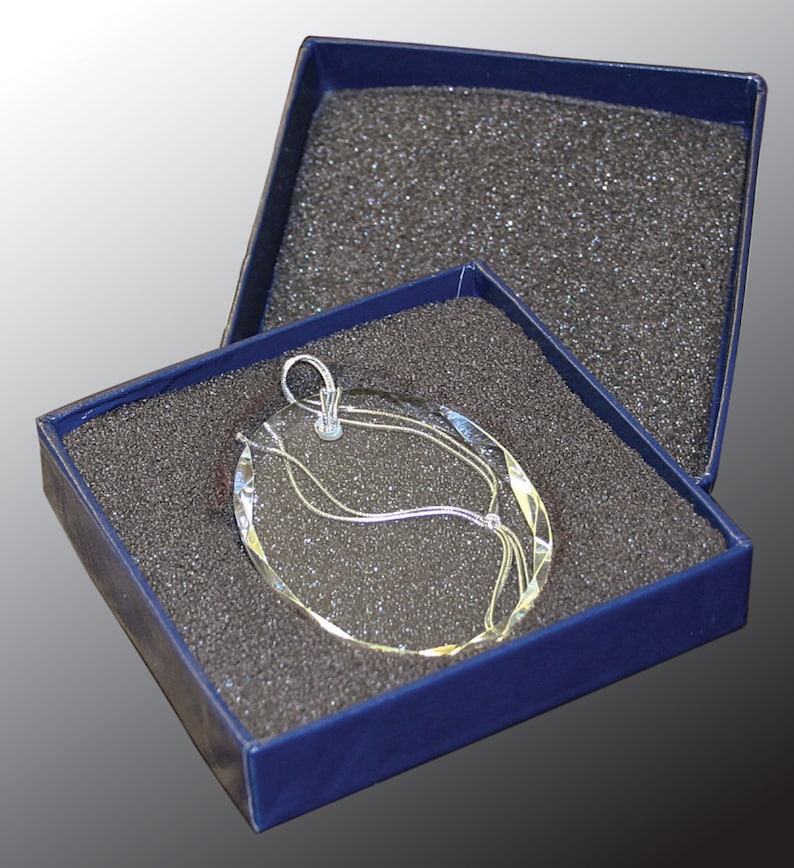 May include: A silver glass ornament with a swirling design is displayed in a blue velvet box with a black foam interior.