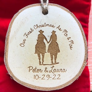 May include: A wooden Christmas ornament with a couple riding horses. The ornament is engraved with the text "Our First Christmas As Mr. & Mrs. Peter & Laura 10-29-22".