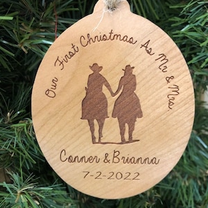 May include: A round wooden ornament with the text "Our First Christmas As Mr. & Mrs. Conner & Brianna 7-2-2022" and a silhouette of two people in cowboy hats.