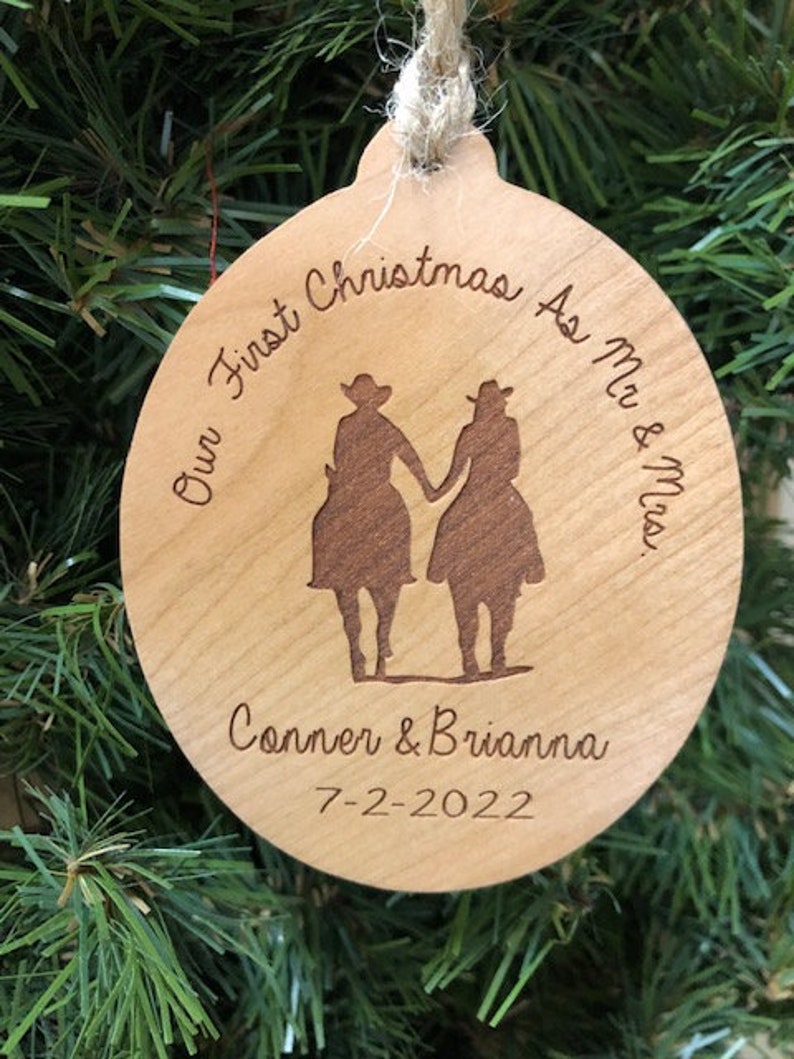 May include: A round wooden ornament with the text "Our First Christmas As Mr. & Mrs. Conner & Brianna 7-2-2022" and a silhouette of two people in cowboy hats.