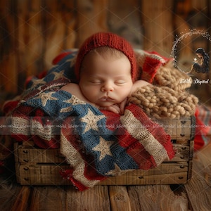 May include: A sleeping infant wearing a red knit cap, resting inside a wooden crate lined with a textured blanket featuring a red, white, and blue star and stripe pattern. A tan chunky knit fabric is tucked beside the infant's head.
