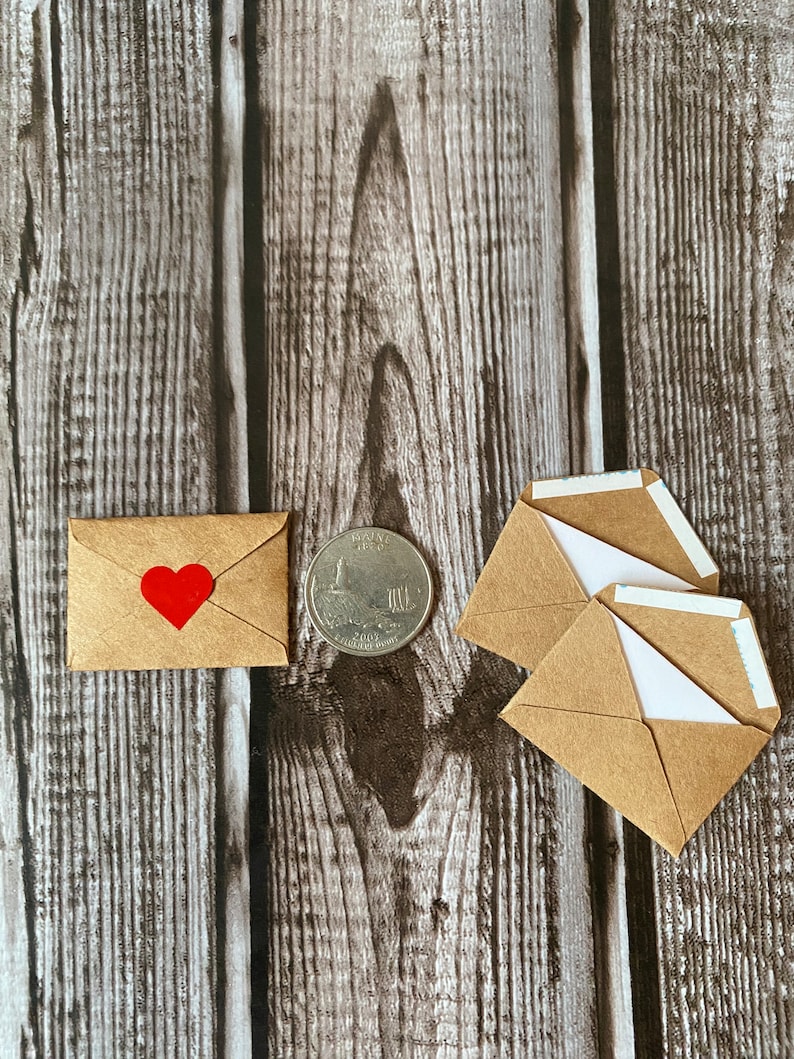 May include: Three small brown paper envelopes with white paper lining and a single envelope with a red heart on the front. A silver US quarter is also in the image.