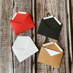 May include: Four small envelopes in different colors: red, black, white, and brown. Each envelope has a white adhesive strip on the flap.