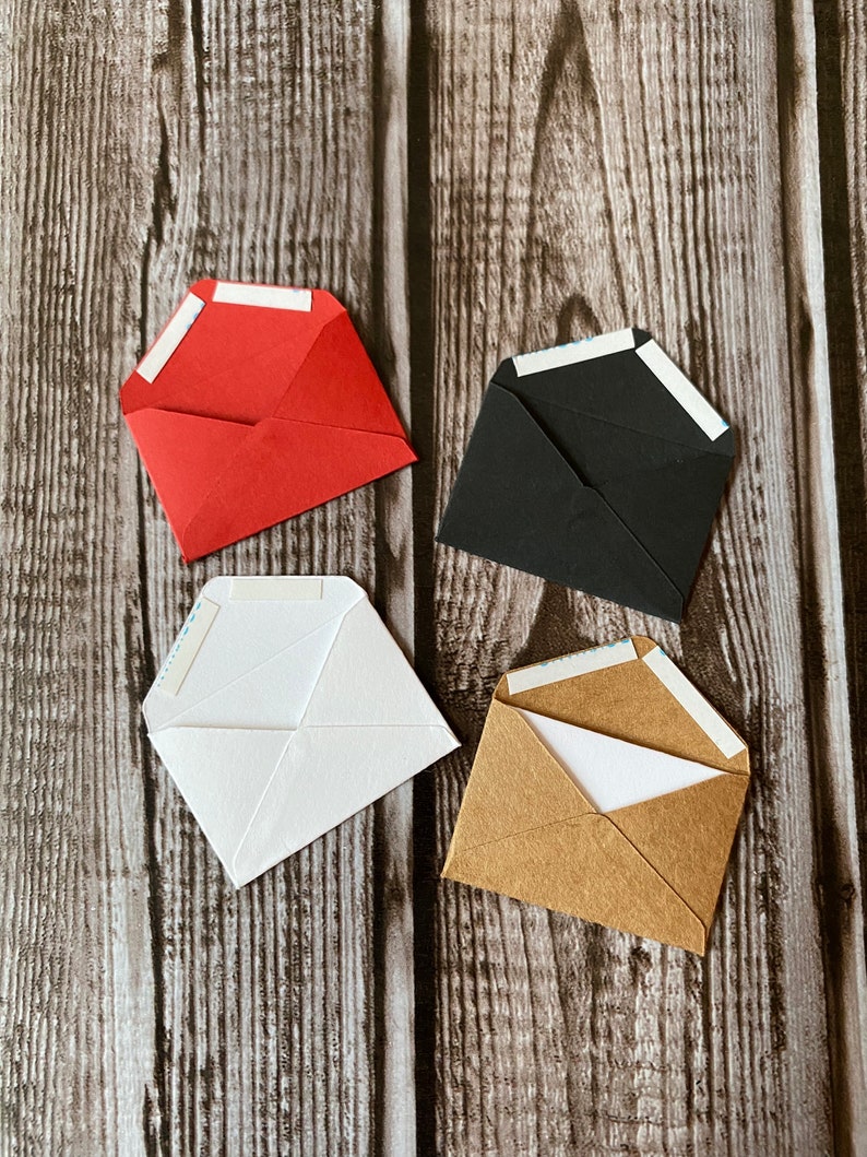 May include: Four small envelopes in different colors: red, black, white, and brown. Each envelope has a white adhesive strip on the flap.