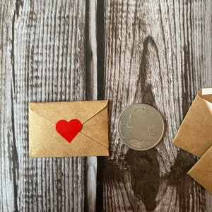 May include: A small brown envelope with a red heart sticker on the front. The envelope is next to a US quarter.