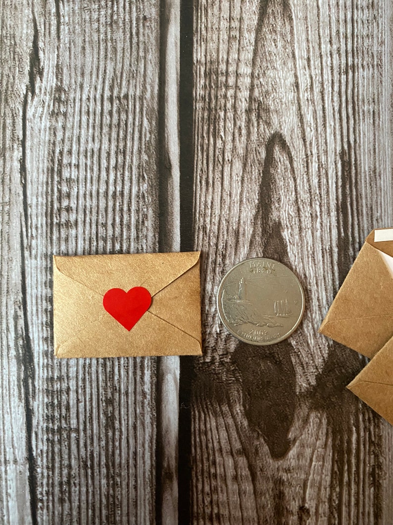 May include: A small brown envelope with a red heart sticker on the front. The envelope is next to a US quarter.