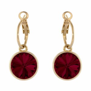 May include: A pair of gold-toned hoop earrings. Each earring features a round, faceted, deep red gemstone pendant. The pendants are set in a gold-colored bezel. The earrings are displayed against a white background.