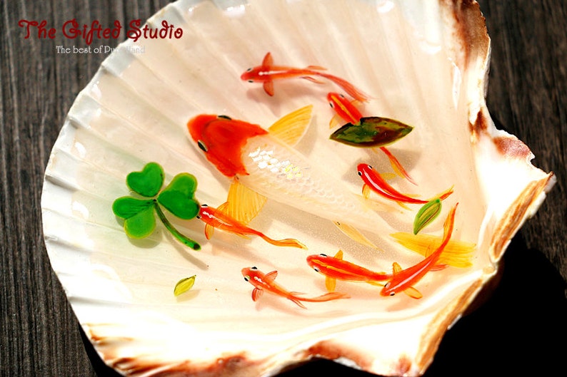 Puede incluir: Una concha decorativa con una escena pintada de peces koi y un tr&eacute;bol. Los peces son naranjas y blancos, nadando en resina transparente. La concha es blanca con bordes marrones. The Gifted Studio.