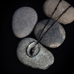 May include: A silver necklace with a black fish pendant resting on gray stones.