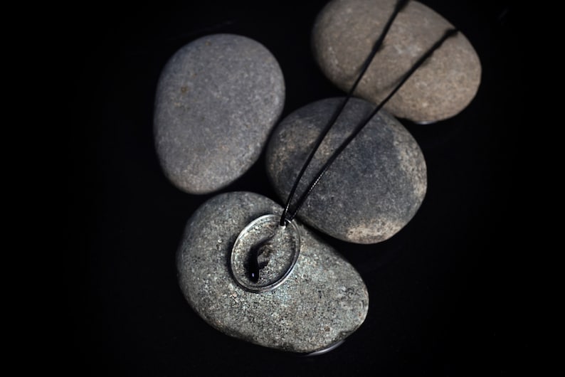 May include: A silver necklace with a black fish pendant resting on gray stones.