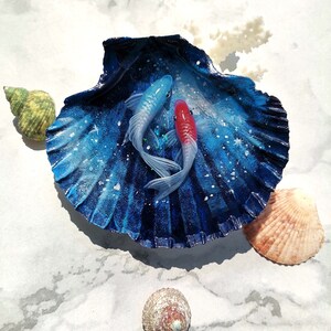 May include: A blue and white seashell with a painted galaxy design and two fish, one blue and one red, inside.
