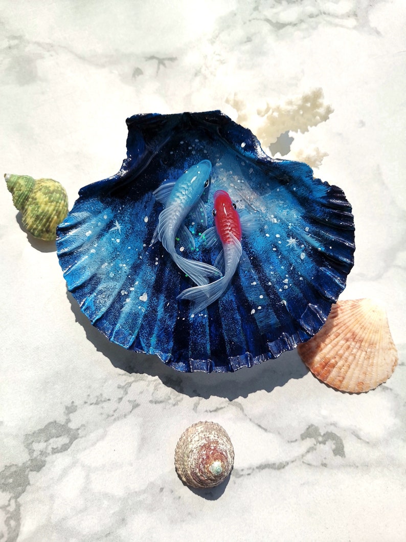 May include: A blue and white seashell with a painted galaxy design and two fish, one blue and one red, inside.