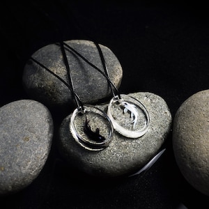 May include: Two black cord necklaces with circular pendants featuring a black and white fish design. The necklaces are displayed on gray stones.