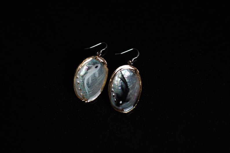 May include: A pair of gold-toned earrings with a white and black fish design on a mother-of-pearl background.