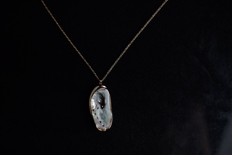 May include: A gold chain necklace with a white seashell pendant.