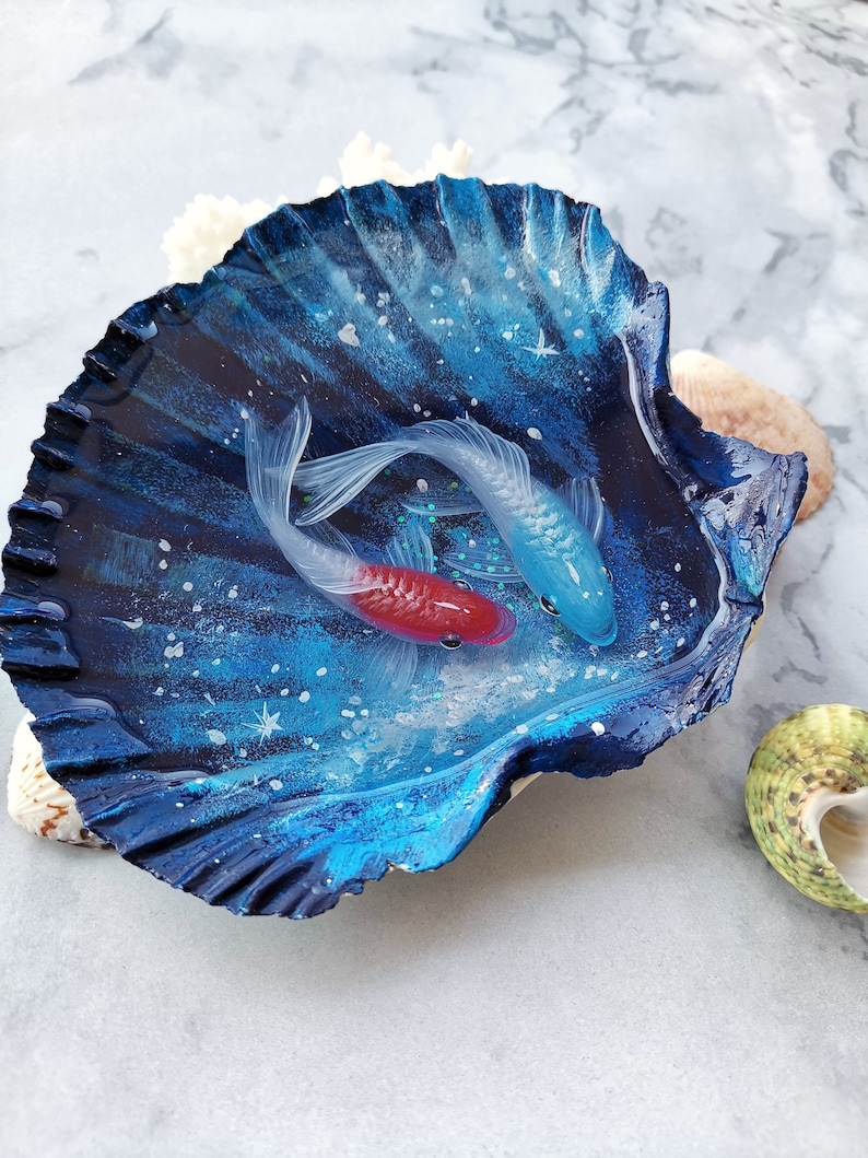 May include: A seashell with a blue and white galaxy design, filled with resin and two painted fish, one red and one blue.