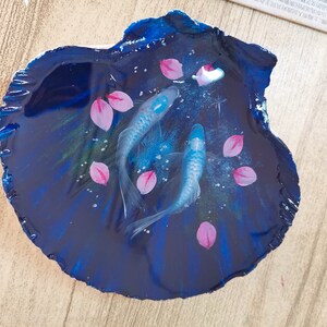 May include: A resin art piece featuring two blue fish swimming in a dark blue, swirling background with pink flower petals.