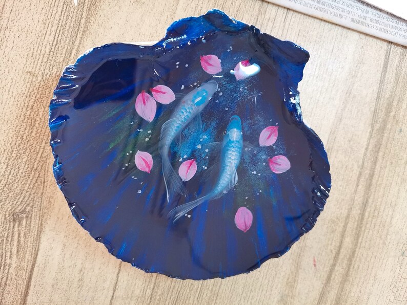 May include: A resin art piece featuring two blue fish swimming in a dark blue, swirling background with pink flower petals.