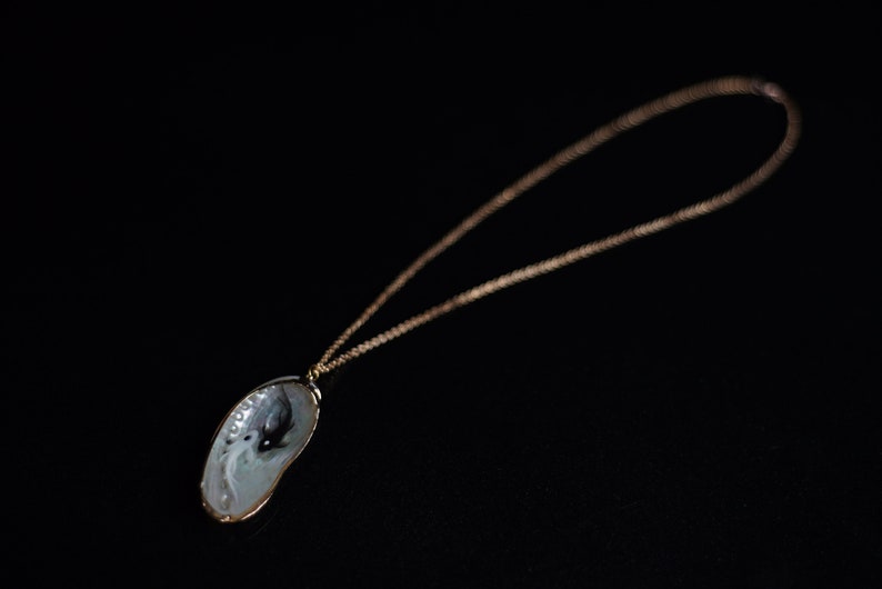 May include: A gold chain necklace with a pendant made from a seashell. The seashell is white with a black and white design inside.