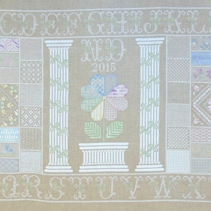 May include: Cross-stitch sampler featuring the alphabet, a flower design, and the text "NED 2015".
