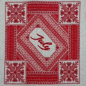 Pode incluir: Bordado de ponto cruz vermelho e branco com a palavra "Julho" no centro.