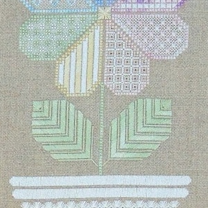 Pode incluir: Um bordado de ponto cruz de uma flor com seis pétalas em diferentes cores e padrões, com um caule e folhas verdes, e uma base branca.