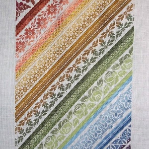 Puede incluir: Un sampler de punto de cruz con un patrón diagonal de puntadas de bordado de colores. Las puntadas están dispuestas en un patrón de arcoíris, con rojo, naranja, amarillo, verde, azul, índigo y violeta.