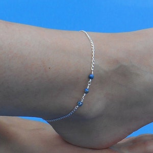 May include: A silver anklet with three blue beads. The anklet is on a person's ankle.