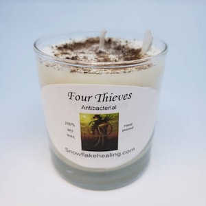 May include: A white candle in a clear glass jar with a label that reads "Four Thieves Antibacterial 100% soy wax Hand poured snowflakehealing.com".