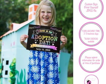 May include: A rectangular black sign with colorful text that reads Today is my Adoption Day, Kailee Maleah, and July 12, 2023. The sign features a banner graphic at the top and a ribbon graphic at the bottom with white heart accents.
