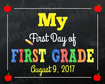 Może przedstawiać: Czarna tablica z białą ramką i tekstem "My First Day of FIRST GRADE August 9, 2017". Tekst jest w kolorowych, obwiedzionych literach. W rogach tablicy znajdują się czerwone jabłka.