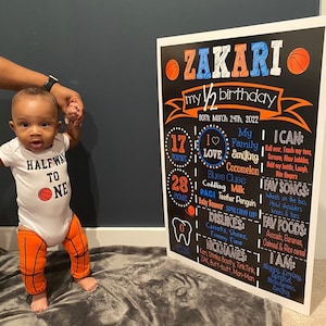 May include: A chalkboard sign with the text "Zakari my 1/2 birthday" and details about the child's first six months, including weight, height, favorite foods, songs, and activities. The sign is decorated with a basketball theme.