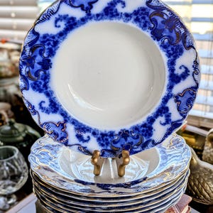 May include: A stack of antique white and blue patterned bowls with gold trim. The bowls have a scalloped edge and a detailed blue design around the rim. The bowls are stacked on top of a red book.