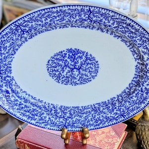 May include: Oval serving platter with a white center and a blue tree branch pattern. The rim and center of the platter feature a detailed blue design. The platter is displayed on a gold-colored stand.
