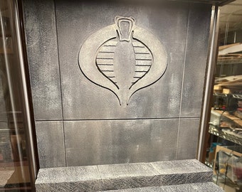 Può includere: Un espositore in cemento grigio con tre gradini. L'espositore presenta un emblema di Cobra in rilievo sulla parete posteriore.
