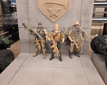 Può includere: Tre action figure di soldati con armi sono in piedi su una piattaforma grigia di fronte a un emblema beige. Le figure indossano uniformi militari e imbracciano fucili. L'emblema presenta un uccello e una stella.