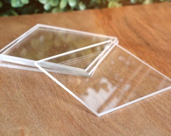 May include: A stack of four clear glass coasters, arranged on a wooden surface.