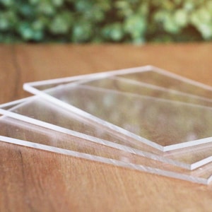 May include: Four clear acrylic sheets stacked on top of each other on a wooden surface.