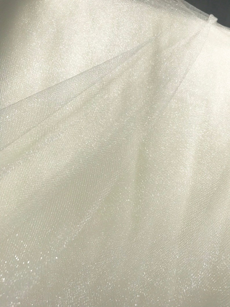 May include: White tulle fabric with a subtle sparkle. The fabric is sheer and has a delicate texture.