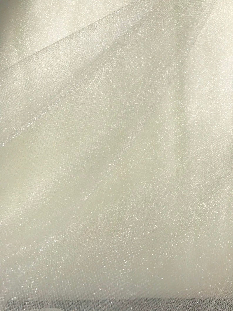 May include: White tulle fabric with a subtle sparkle. The fabric is sheer and has a delicate texture.