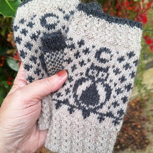 May include: A pair of knitted fingerless gloves with a black and white geometric pattern. The gloves are made of a soft, beige yarn and have a black trim.
