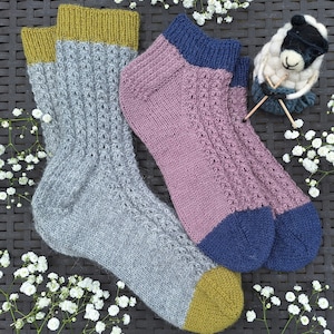 May include: Two pairs of hand-knitted socks with contrasting colored toes and heels. One pair is gray with a yellow cuff and the other is pink with a blue cuff.