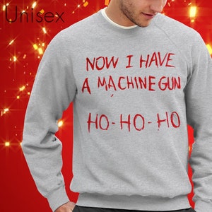 May include: A grey sweatshirt with the text "NOW I HAVE A MACHINE GUN HO-HO-HO" printed in red.