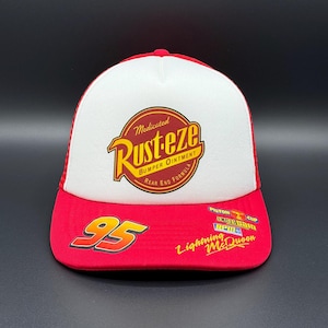 May include: Red and white trucker hat with the text "Rust-eze" and the number "95". The hat has a mesh back and a curved peak. The design includes the words "Bumper Ointment" and "Rear End Formula".