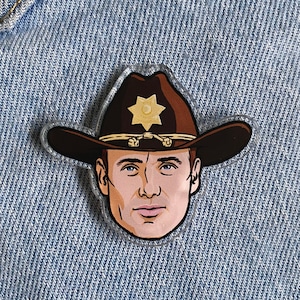 Puede incluir: Un sombrero de sheriff marrón y negro con una insignia de estrella dorada. El sombrero está sobre un fondo de mezclilla azul.