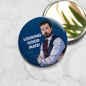 Può includere: Uno specchio compatto blu con un'illustrazione di cartone animato di un uomo con la barba e il testo "LOOKING GOOD MATE!" sul davanti.