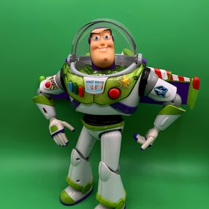 May include: A Buzz Lightyear action figure, featuring a white and green spacesuit with purple accents. The figure has a clear helmet, a smiling face, and the words "SPACE RANGER" on the chest. The figure is standing against a green background.