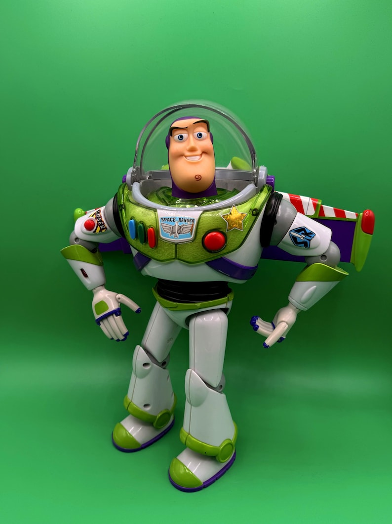 May include: A Buzz Lightyear action figure, featuring a white and green spacesuit with purple accents. The figure has a clear helmet, a smiling face, and the words "SPACE RANGER" on the chest. The figure is standing against a green background.