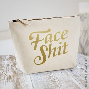 May include: A white canvas zippered pouch with a gold inscription that reads "Face Shit".