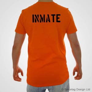 Puede incluir: Una camiseta naranja brillante con la palabra "INMATE" impresa en negro en la espalda.